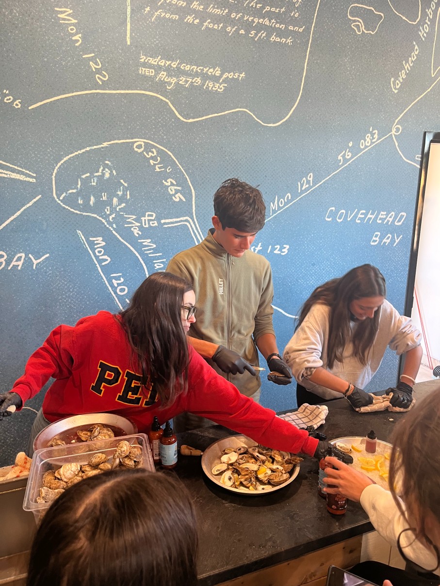 Three young people wearing black gloves shucking oysters at a counter.
