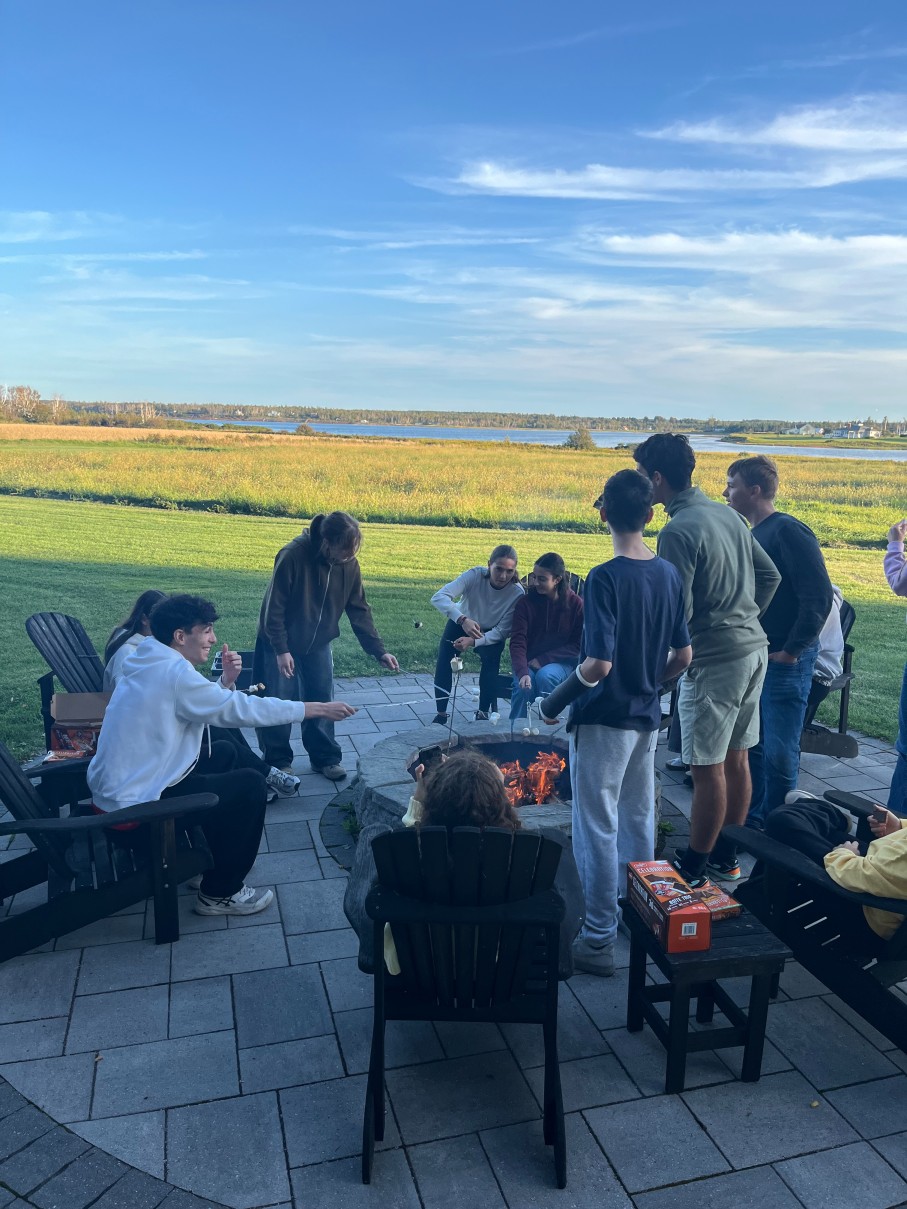 A group of students roasting marshmallows around an outdoor fire pit.