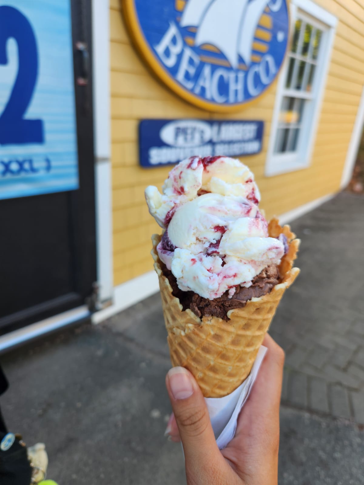 Hand holding an ice cream cone with chocolate and berry-swirl scoops