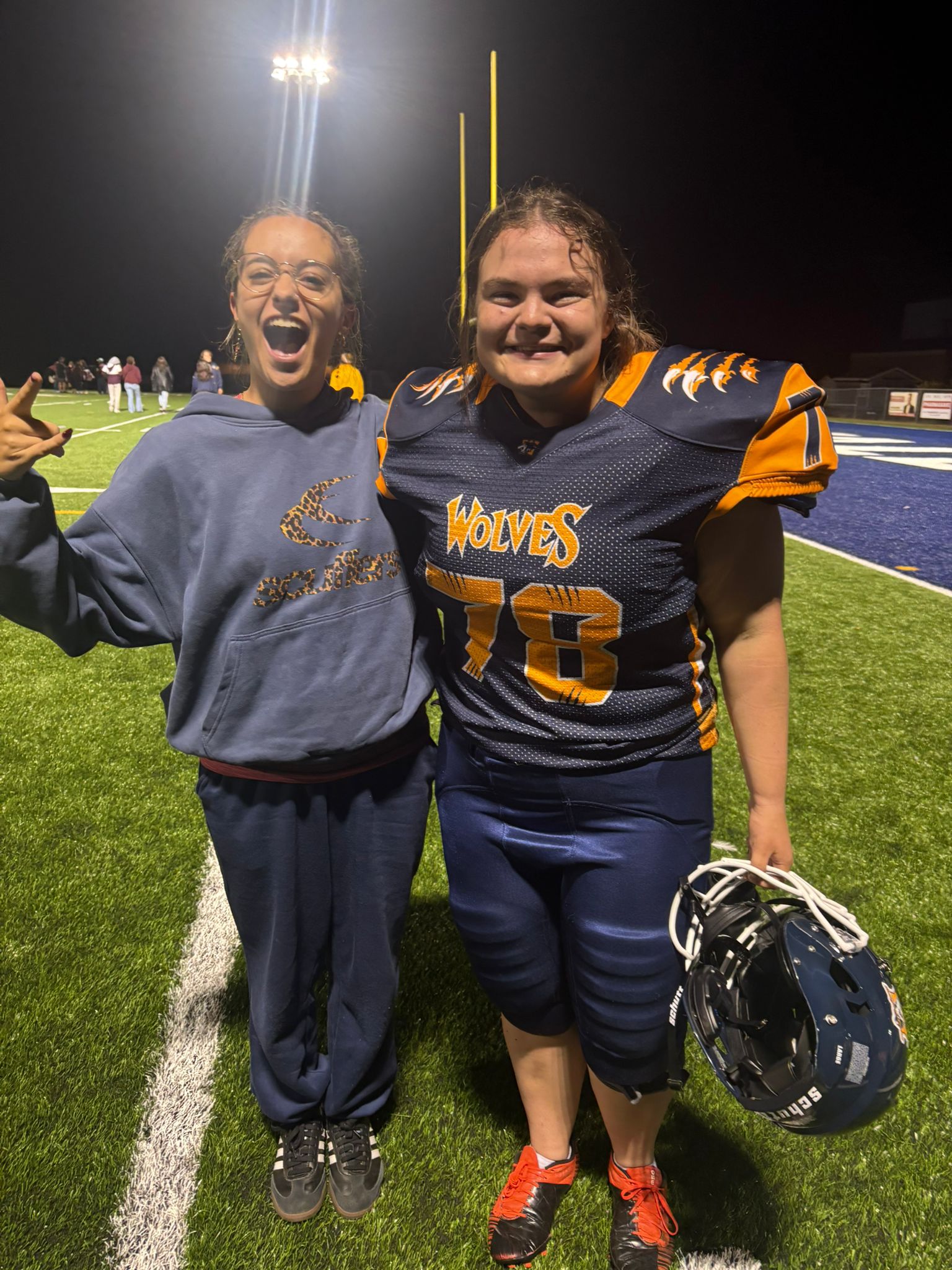 Two people standing on a football field at night with stadium lights